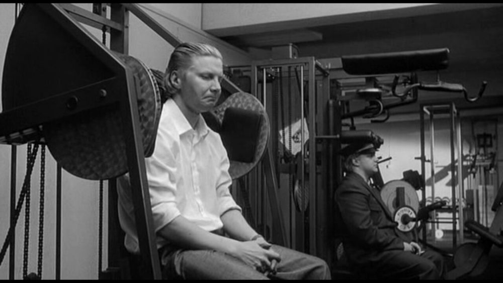 Ein Film-Still aus Hamlet Goes Business
Hamlet sitzt auf einem Fitness-Gerät und zieht die Mundwinkel nach unten 