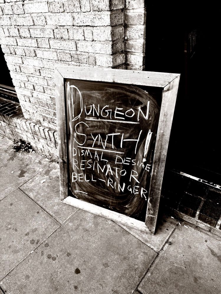 Chalkboard sign outside the Post Bar, reading “dungeon synth dismal desire resinator bell-ringer”