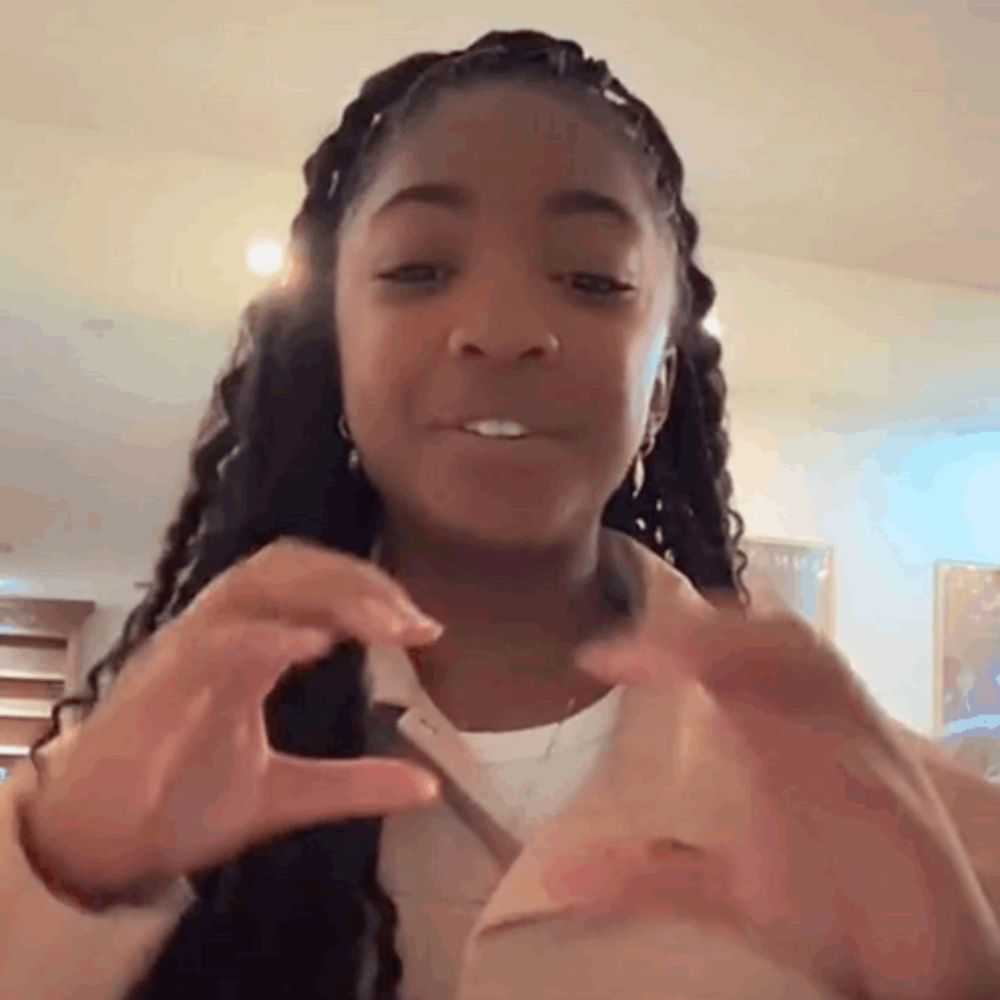 a young girl is making a heart shape with her hands and smiling .