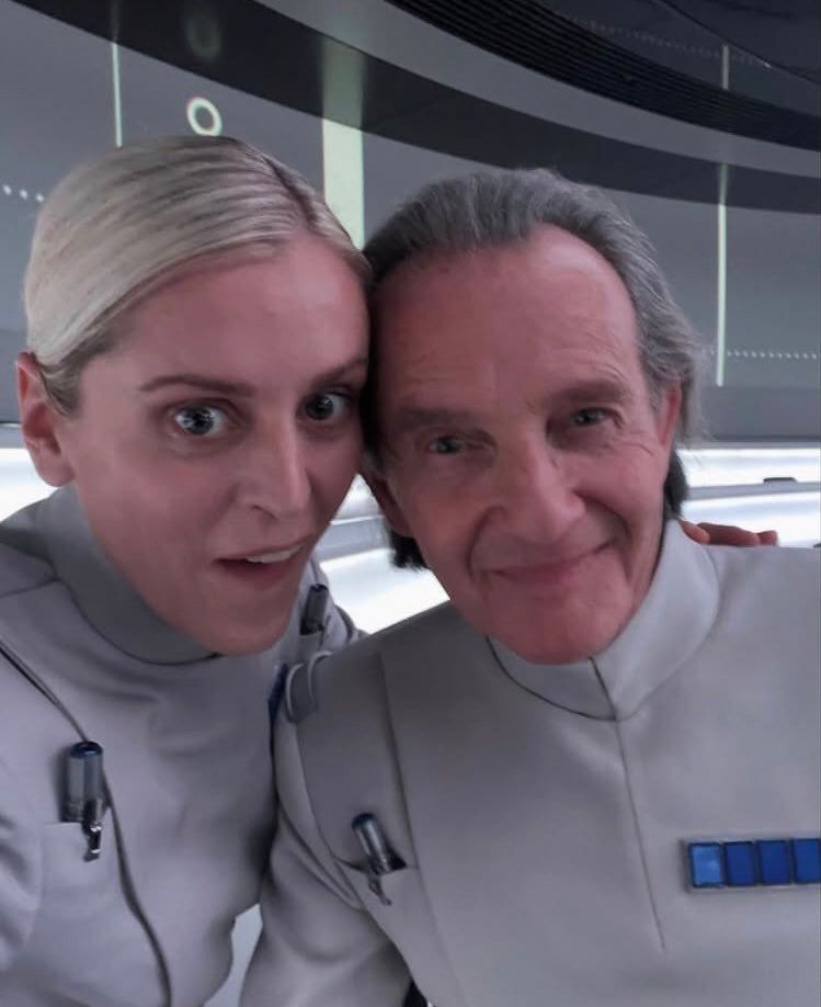 Dedra and Partagaz posing in costume on the set of Andor, warm goofy expressions 