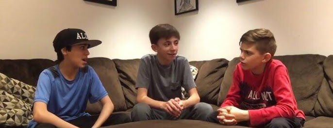 Three young boys sitting on a couch discussing things