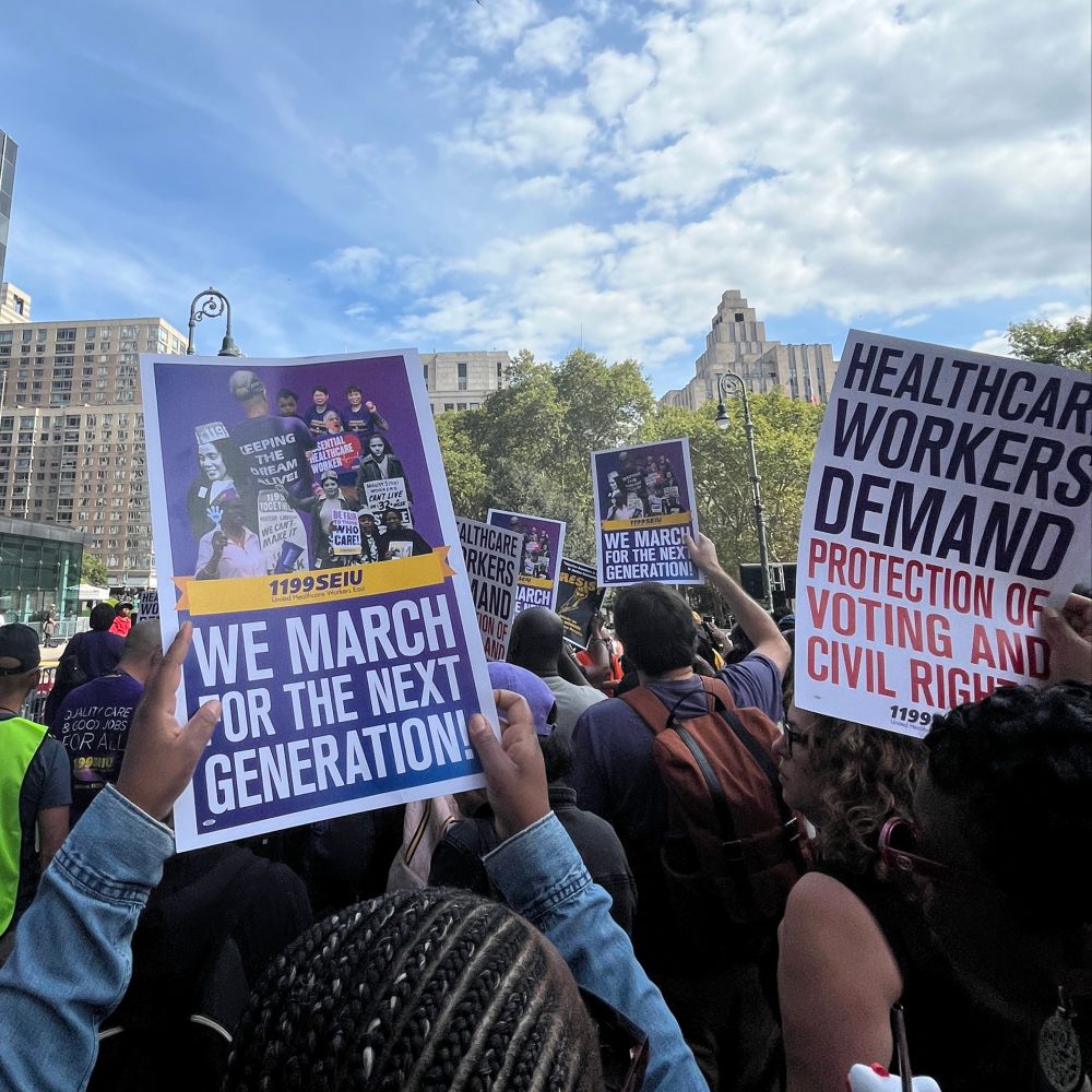 A photo of 1199ers at the August 28, 2025 March on Wall Street to commemorate the original March on Washington and fight for a better future. They are holding signs that read, 