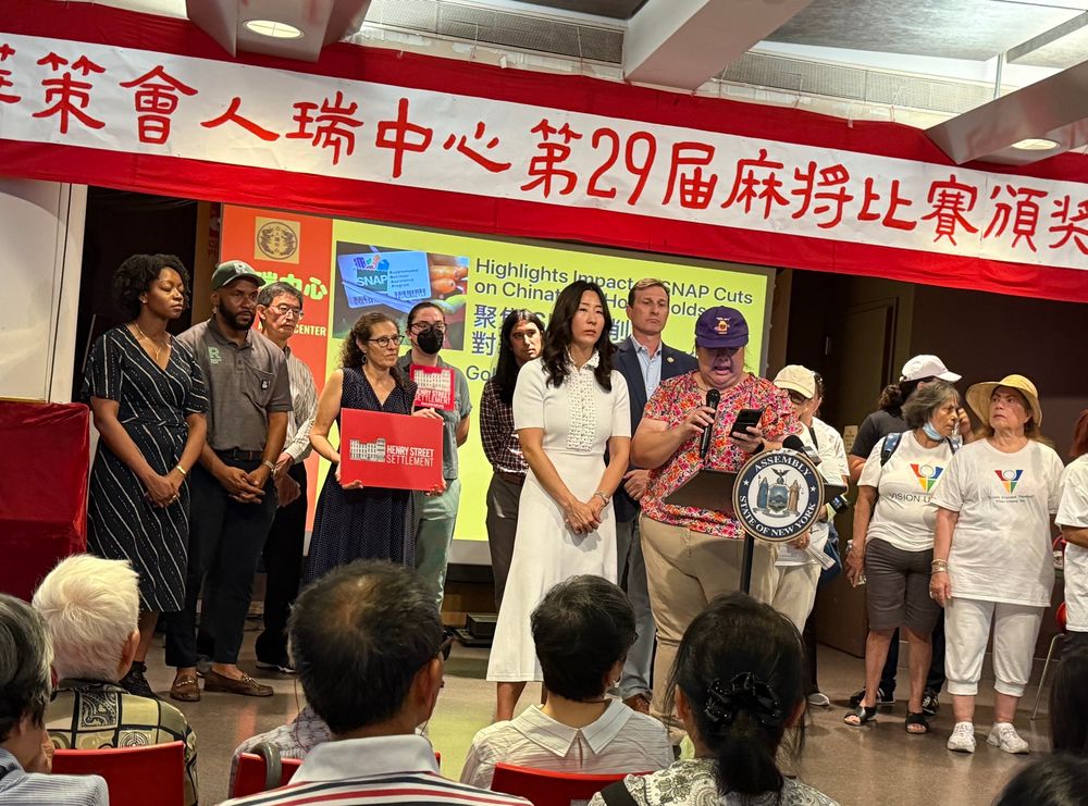 a photo of a press conference held at the Chinese-American Planning Council’s Older Adult Center in NYC Chinatown on the impact of federal funding cuts to SNAP. on stage are NY Congressman Dan Goldman, NY Assemblymember Grace Lee, and 1199 delegate Yan N. Looi wearing a purple 1199 homecare hat. 