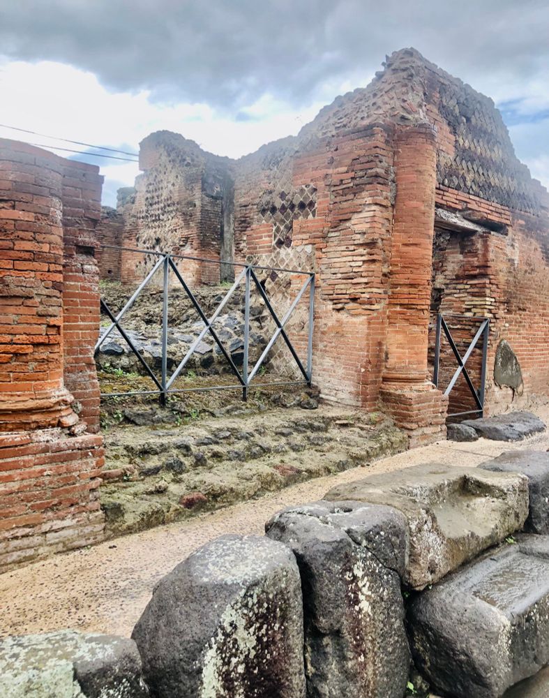 Crumbling walls .Thin red bricks, some metal gates. large boulders at the front. 