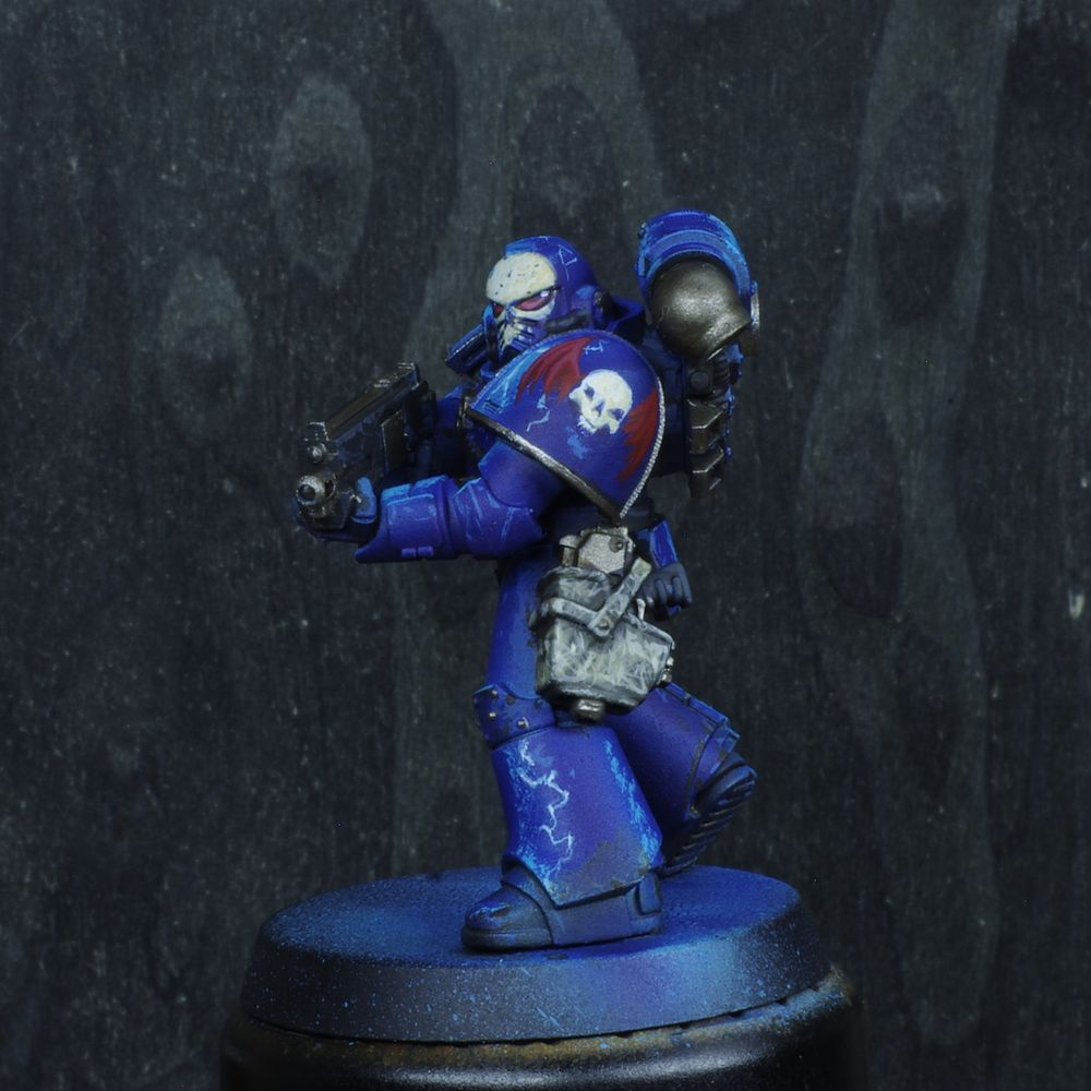 Photo d'une figurine de space marine de warhammer 30000 l'hérésie d'horus. Iel est un Night Lords, son armure est bleu nuit avec des reflets bleu électrique. Son casque a un crane déssiné dessus. Il ya de nombreux motifs d'éclairs désinées sur son armure.