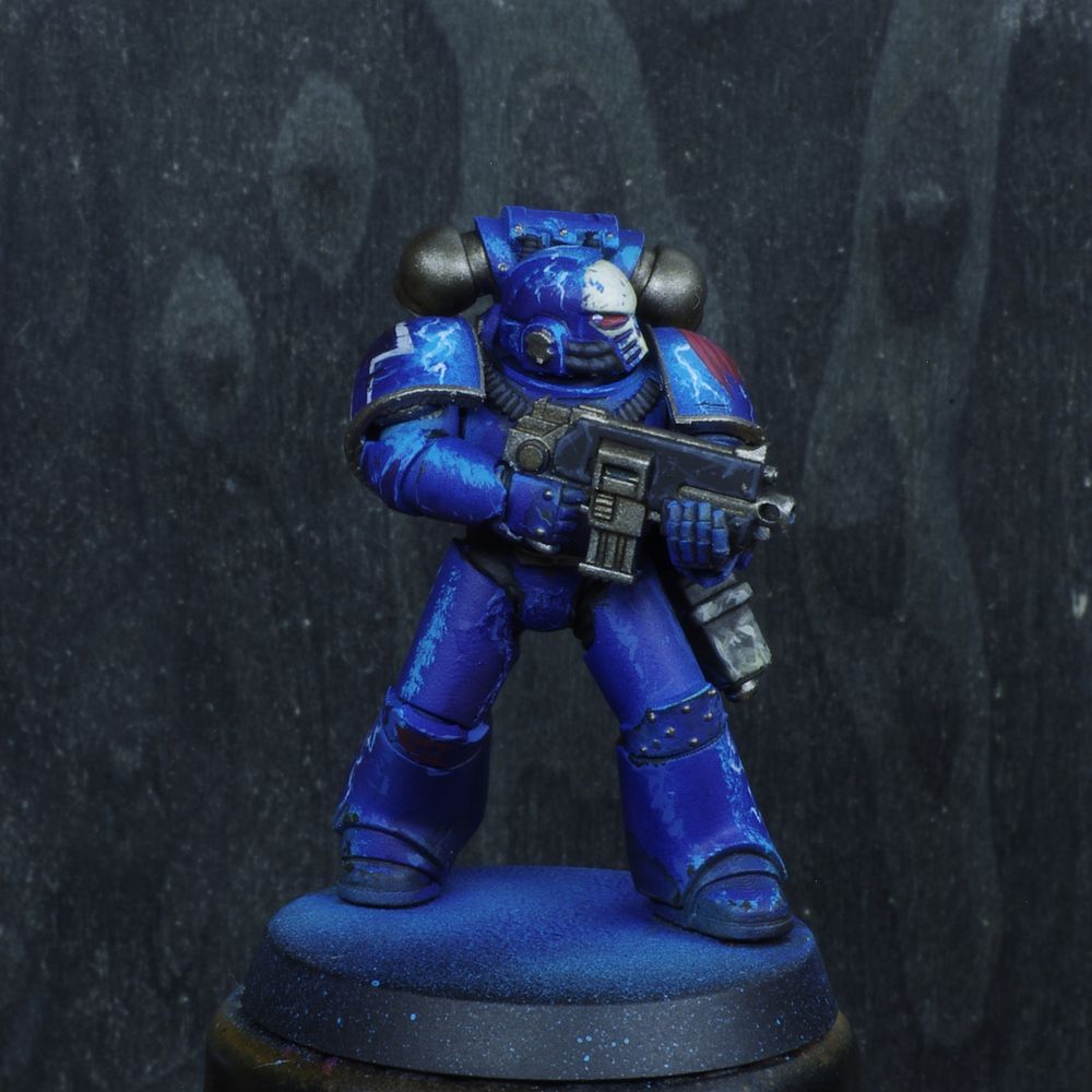 Photo d'une figurine de space marine de warhammer 30000 l'hérésie d'horus. Iel est un Night Lords, son armure est bleu nuit avec des reflets bleu électrique. Son casque a un crane déssiné dessus. Il ya de nombreux motifs d'éclairs désinées sur son armure.