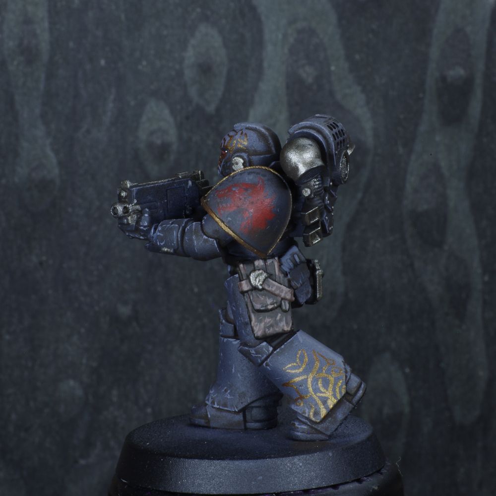 Photo d'une figurine de space marine de warhammer 30000 l'hérésie d'horus. Iel est un Space Wolves, son armure est grise sombre avec des motifs rouges et dorés, elle est usée. 