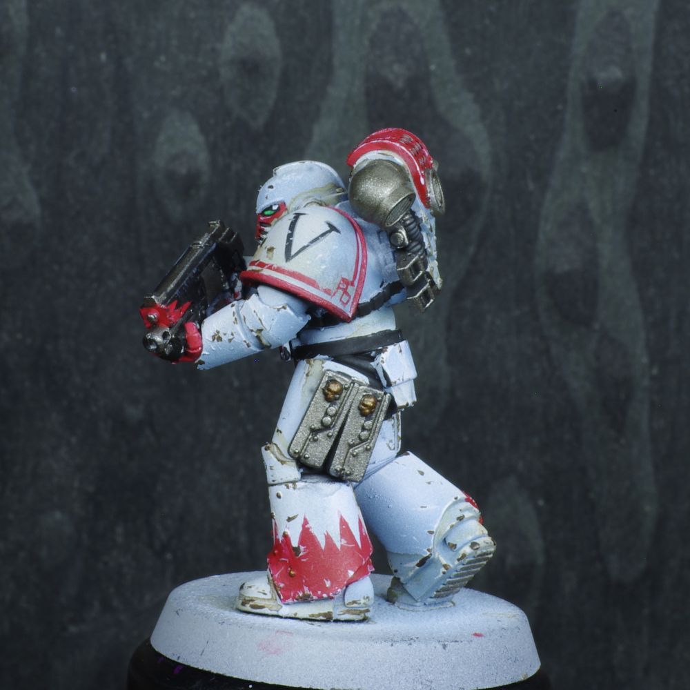 Photo d'une figurine de space marine de warhammer 30000 l'hérésie d'horus. Iel est un White Scars, son armure est blanche avec des motifs rouges, elle est usée. Il ya de nombreux motifs noirs désinées sur son armure.