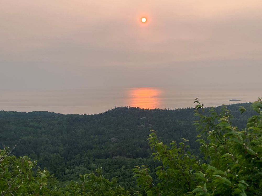 Morning sun reflecting in Lake Superior. There are forested hills in the foreground. 