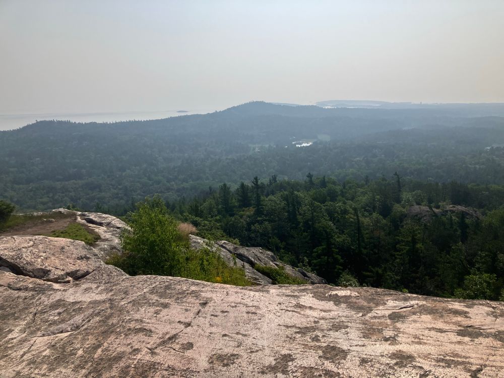 Lake Superior from the top of a mountain. There’s forest before the lake. Everything is covered in wildfire smoke