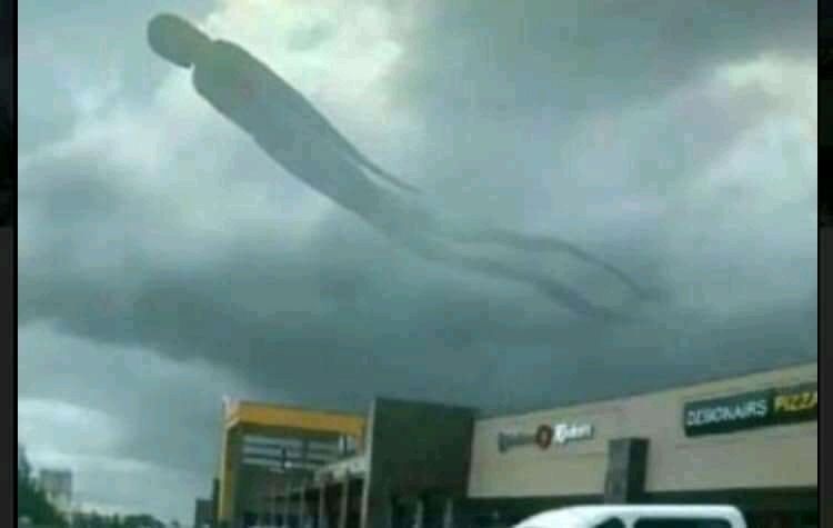 ominous giant shadow entity floating through the clouds over a shopping mall