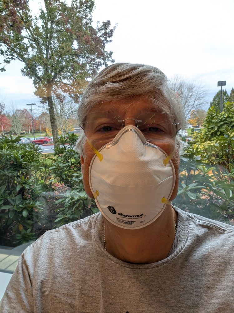Selfie of OP wearing a white N95 mask with trees visible outside the window.