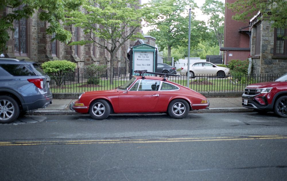Red Porsche parked in front of fence and leafy trees