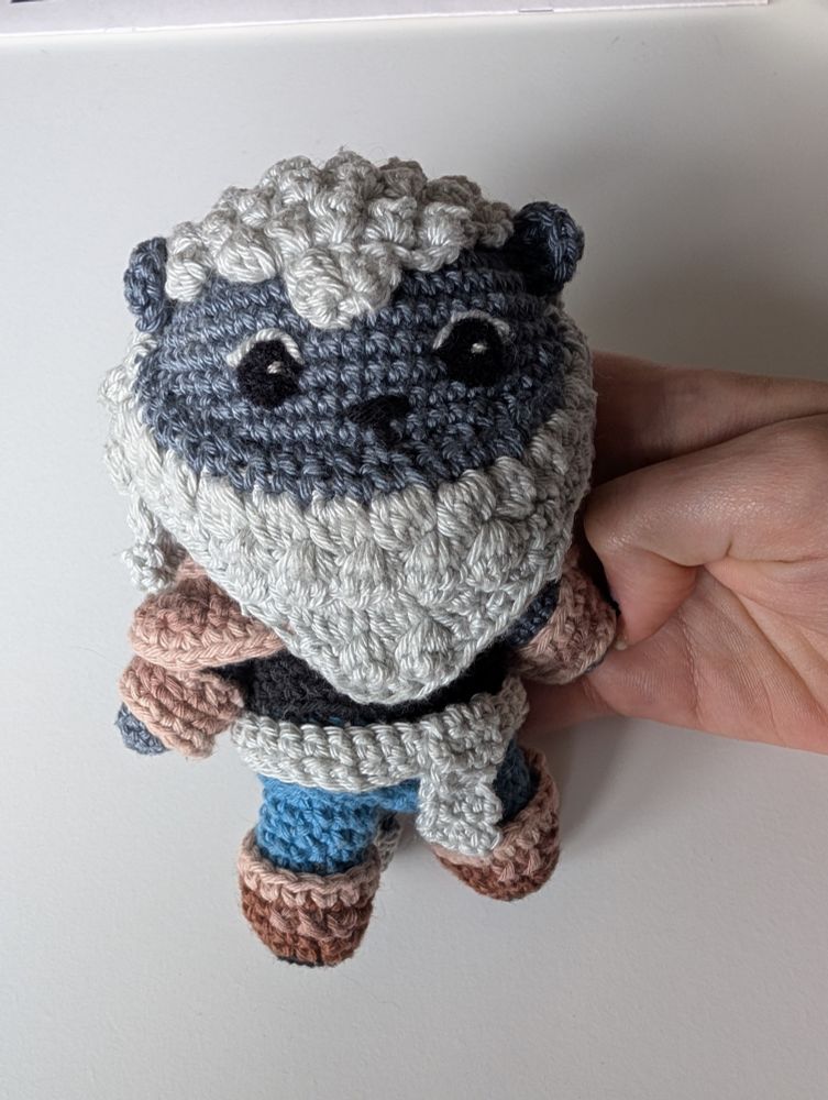 A crochet plushie of a blue lion man with brown boots and a blue belt