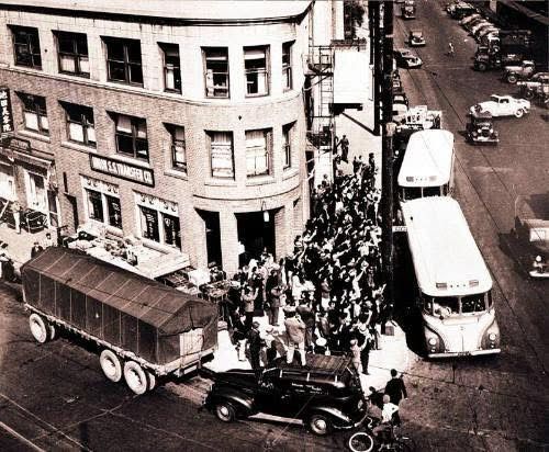 Black and white photograph showing an Aerial perspective of crowd boarding buses in front of Nishi Hongwanji Buddhist Temple, Los Angeles, California, 1942. 