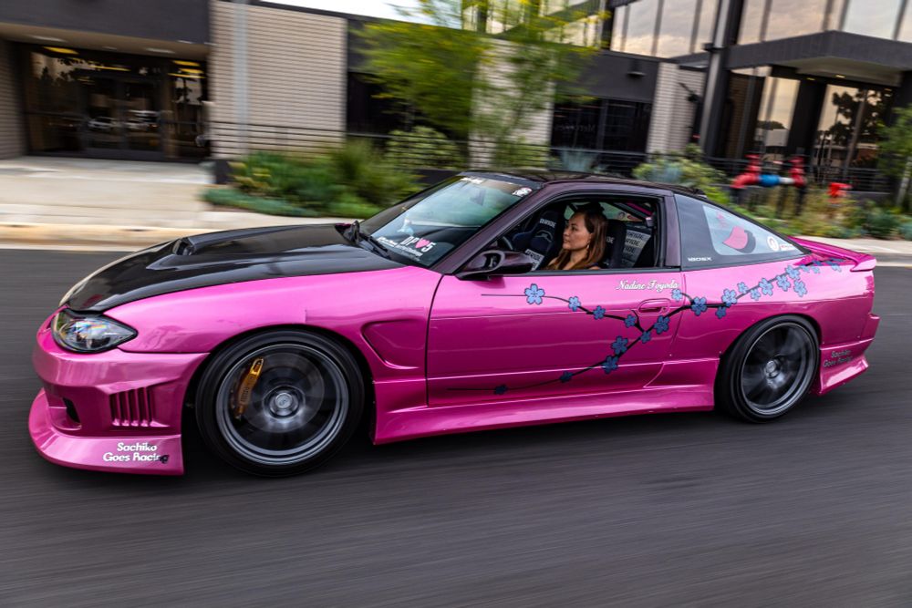 Photo of Nadine Sachiko Hsu’s driving down the street in a hot pink 1989 Nissan 240SX. 