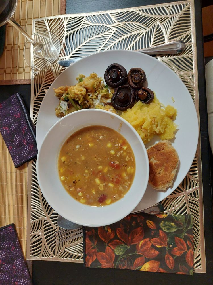 A close up of all the food arranged on a plate, around a bowl of stew. There's an autumn themed napkin beside the plate