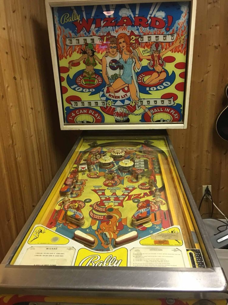 The Wizard pinball machine from 1975 in a room with wood paneling on the walls. 