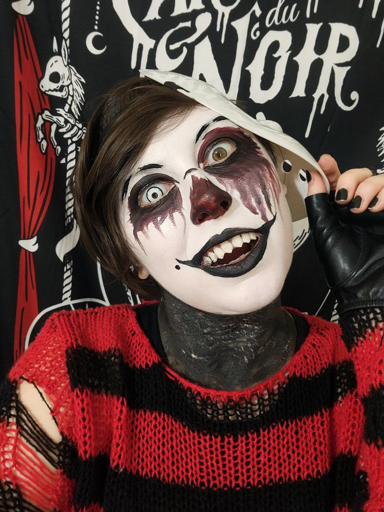 Black and white clown with bloody motifs on his eyes, wearing red and black sweater while holding a hockey goalie mask