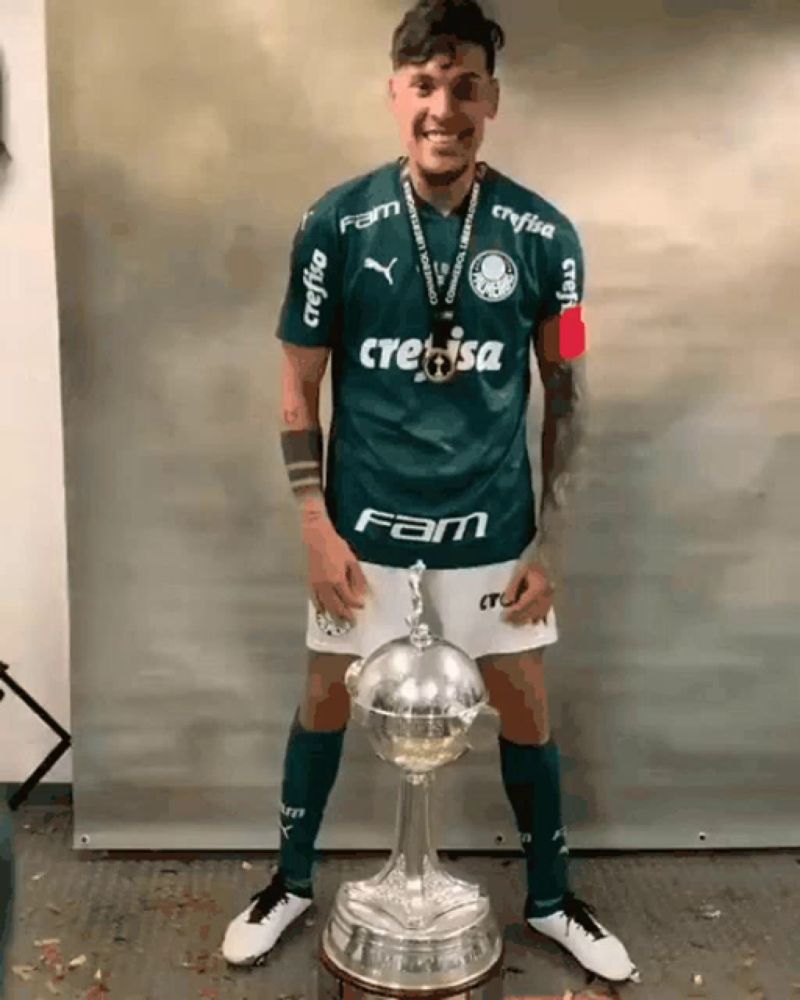 a man wearing a green crefisa jersey stands next to a trophy