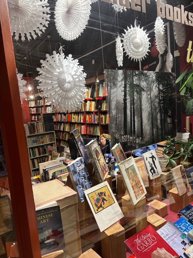 Calder Theatre Bookshop beautifully lit of an early December nights. Brightly coloured books. White paper Christmas decorations.