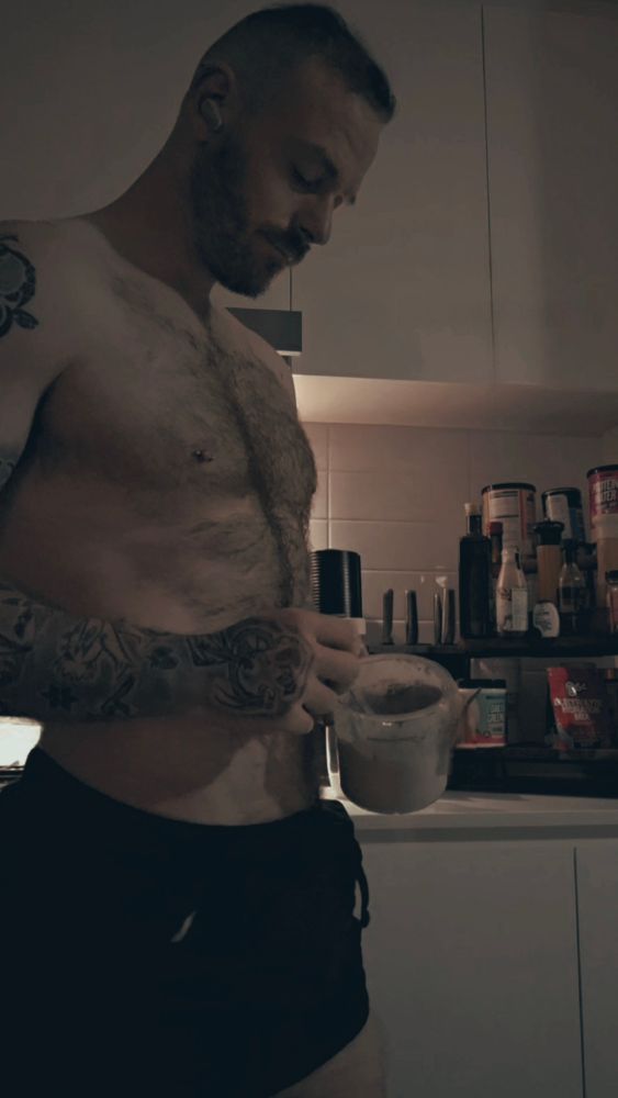 Man shirtless in kitchen eating ice cream 