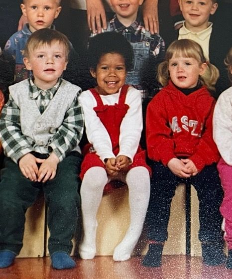 edda in kindergarten with an afro wearing a white shirt and red dress 