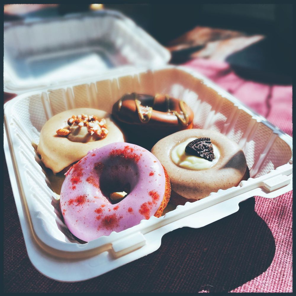 four donuts with elaborate icings and toppings in a white container with the sun shining on them