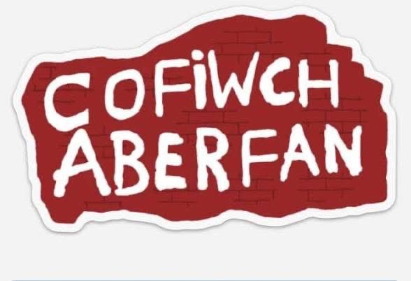 Red on white background with white lettering which says, “Cofiwch Aberfan” which means remember Aberfan. 
