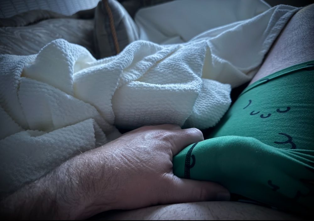 A man’s hand holding his cock through green simpsons boxer briefs in the morning light from bed. 