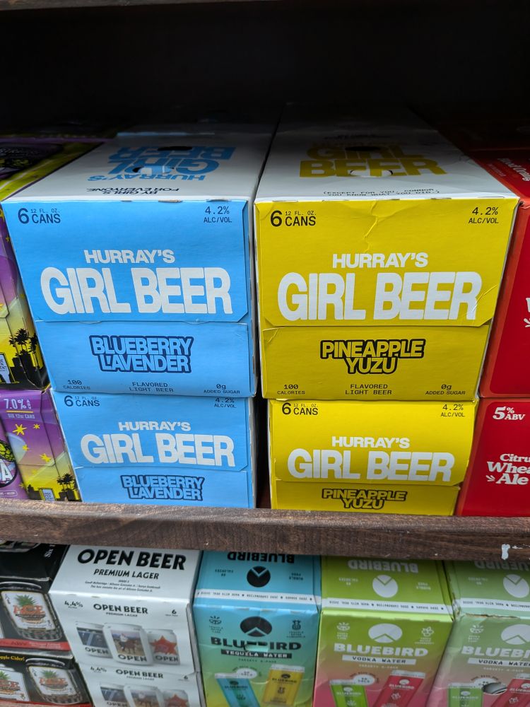 Cardboard 6 packs labeled Girl Beer, 1 blue in Blueberry Lavender flavor and one yellow in Pineapple Yuzu flavor 