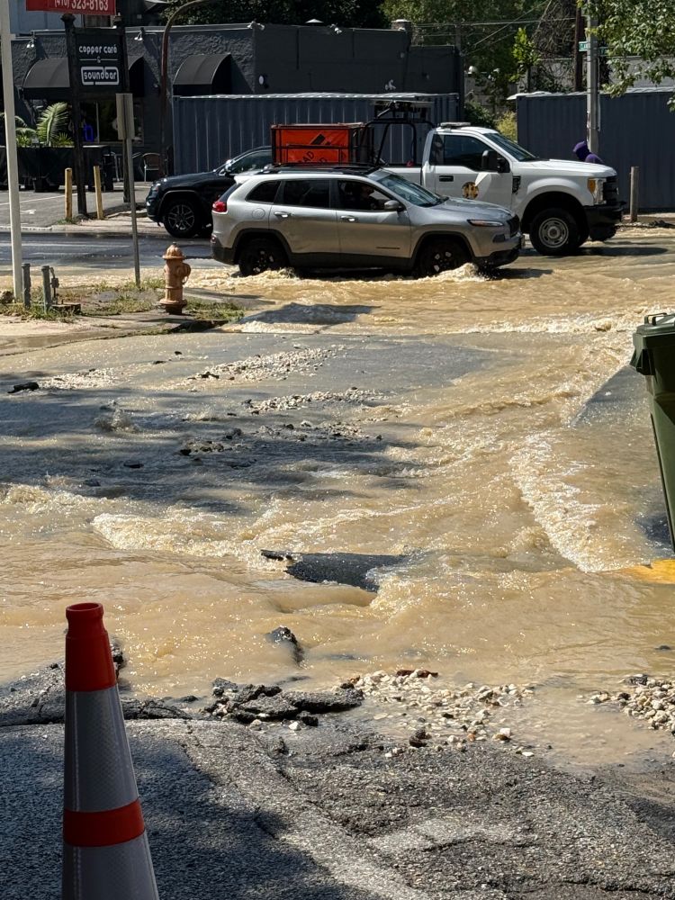 Crumbling Road blocked by cones a river of brown water is flooding into the road below  