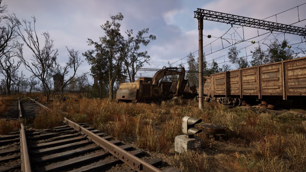A screenshot from STALKER 2 videogame. Two railroad tracks with wooden ties diverge in the shot. Metal cargo box cars are seen on the right along with an old excavator. A semaphore sits on the ground in the foreground.