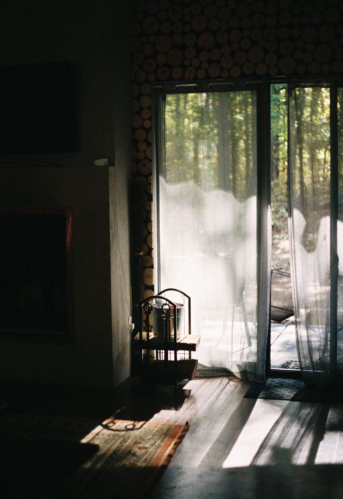 A film photograph of light coming into a cabin through a sliding door near a fireplace