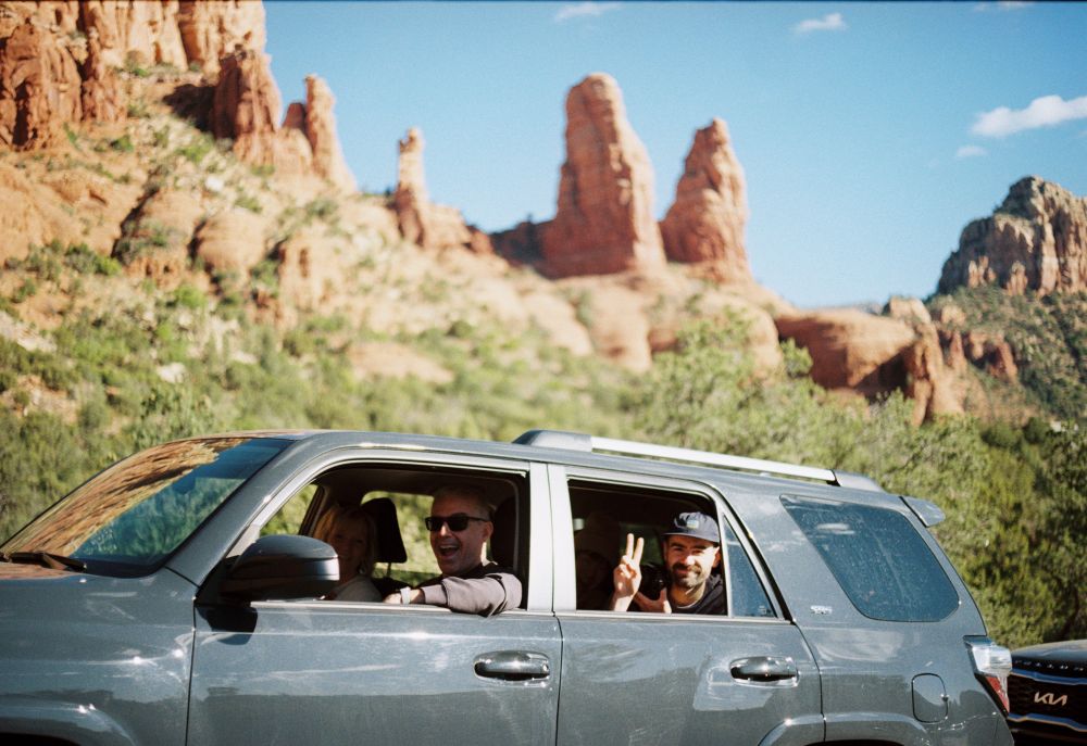 My tiny little brother in the back seat of a Toyota forerunner in Sedona Arizona making a peace sign in front of a large red rock formation that also kinda looks like a peace sign 