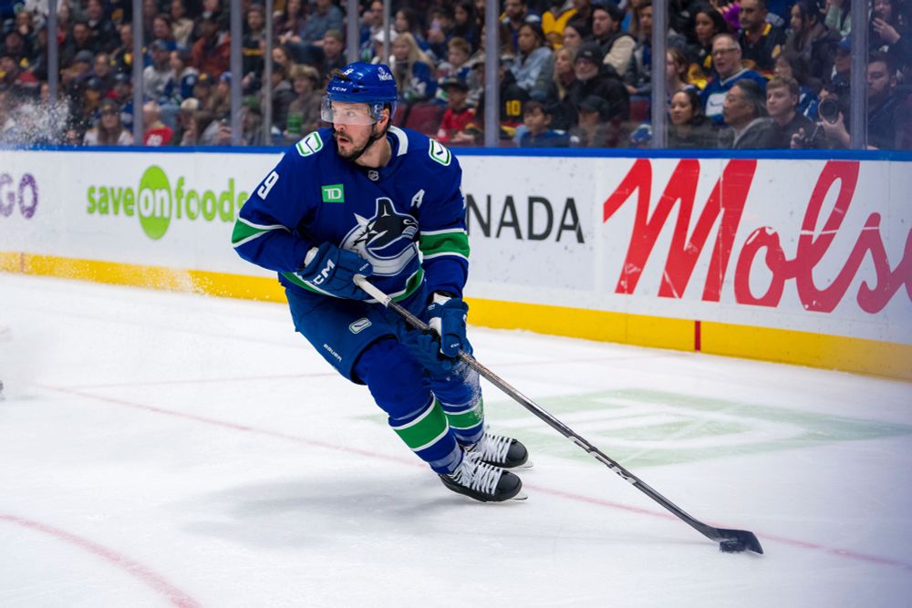 JT Miller with the puck on the bumper wearing the blue canucks jersey.