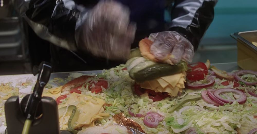 a burger with like 20 slices of cheese and 2 whole pickles surrounded by a whole pile of lettuce, onions and tomato