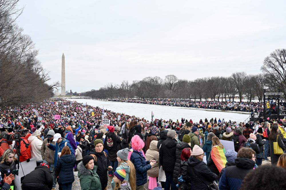 Crowd of people participating in the People's March with various signs, with the Washington Monument visible in the background.