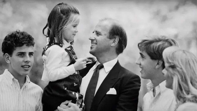 Black and white photo of President Joe Biden smiling with his children and Dr. Biden.