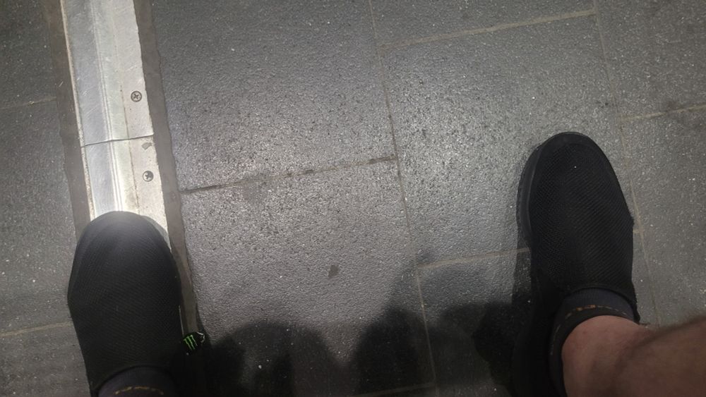Zwei nackte Wadena mit schwarzen stoffschuhen auf grauem betonbiden mit weisser markierungslinie links