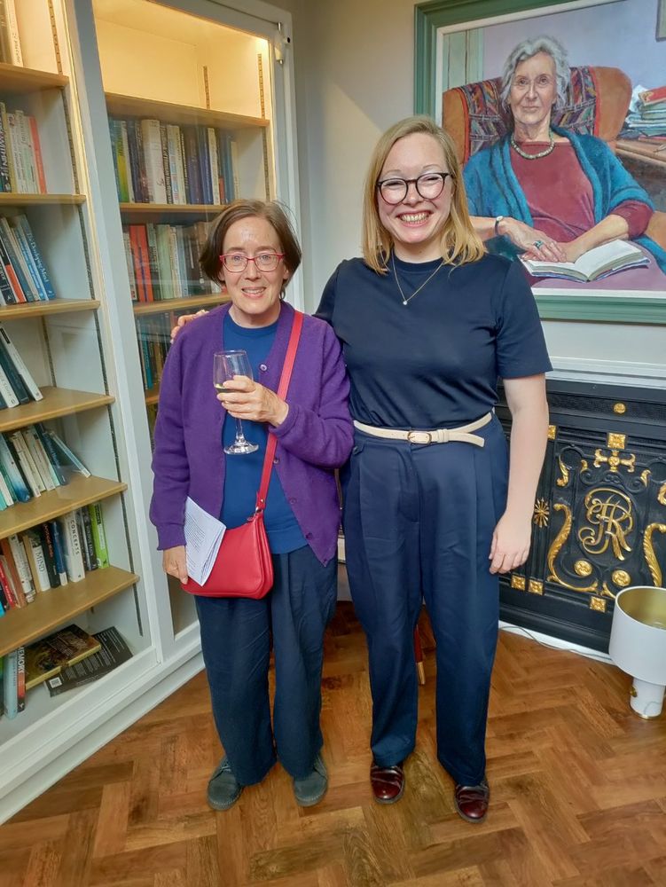 Image of two people standing and smiling in front of a portrait of a person