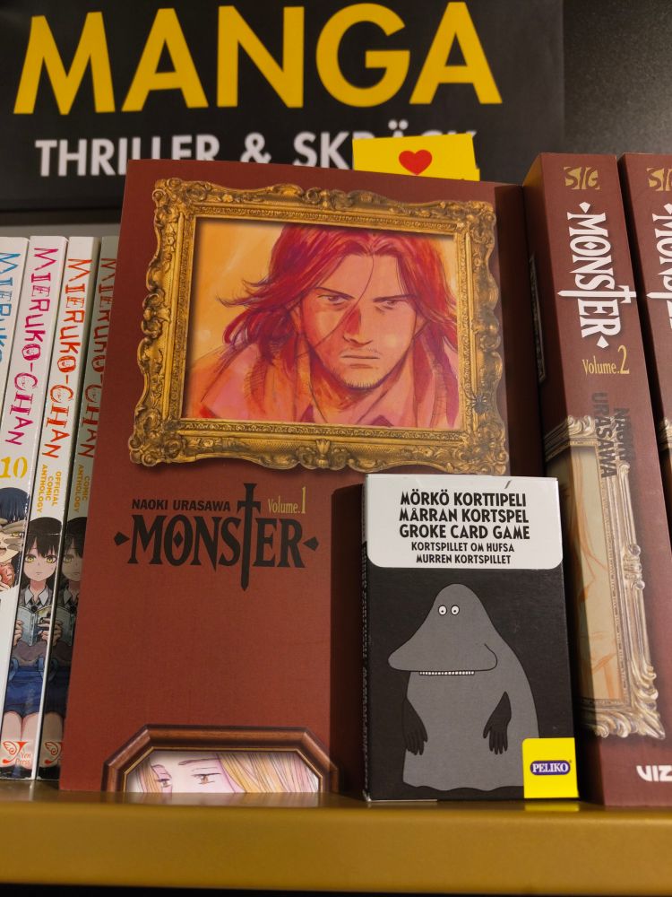 A Groke card game standing on a shelf with the first Monster manga book by Urasawa.