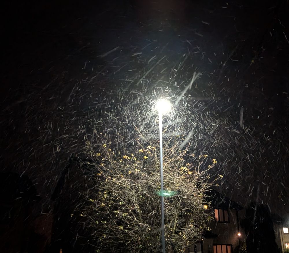 Snow falling in the dark in front of the streetlight