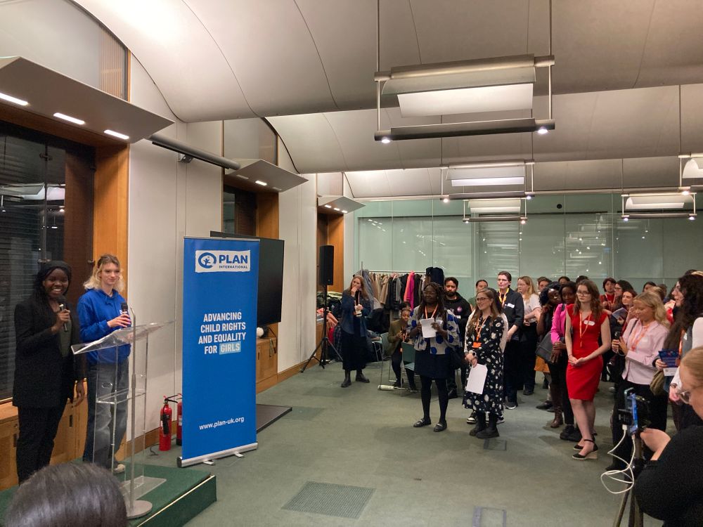 Two young women hold microphones and speak to a crowd of people 