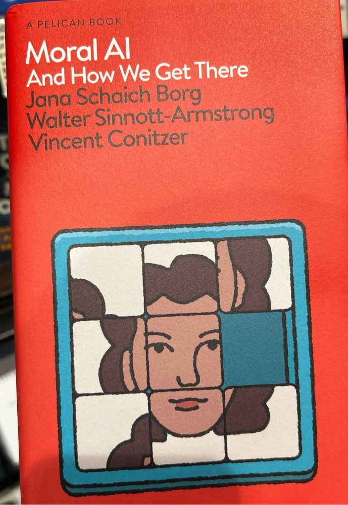 Photo of the book “Moral AI” by Jana Schaich Borg, Walter Sinnott-Armstrong, and Vincent Conitzer. The cover has a red background with white and black text. It features an illustration of a sliding puzzle with a partially completed image of a person’s face, symbolizing the complexity of moral AI. The book is part of the Pelican Books series.