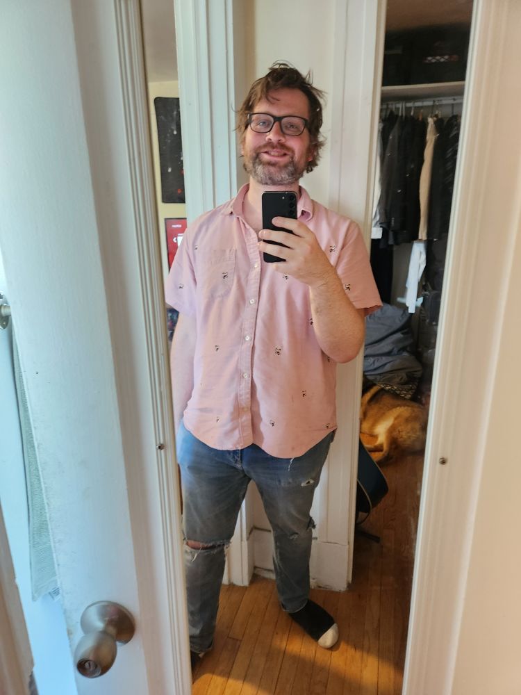 Boy Alex Haus of Decline resembling Dan Harmon, Slavoj Zizek and or Matt Christman. Heavy set, tired looking. Colorful shirt. Ill fitting jeans.