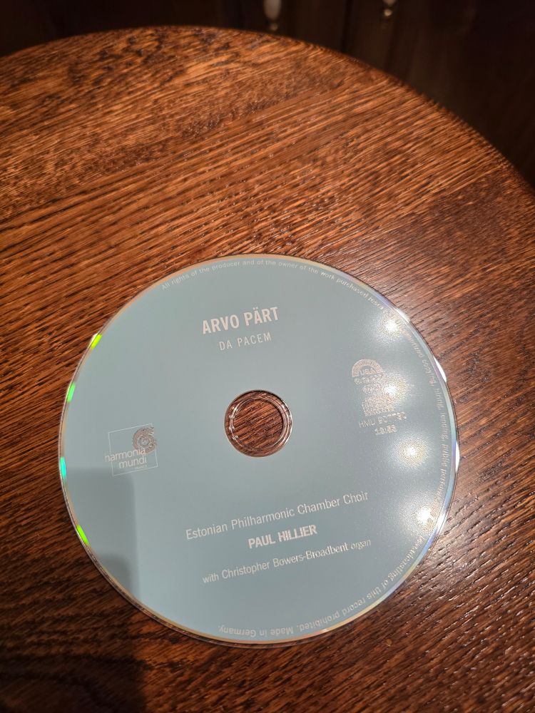 Photo of a music CD Arvo Pärt  Da Pacem 
CD is light blue with white writing and is sitting on a wooden surface.  The lighting is poor with hotspots and shadows because I am a lazy photographer.