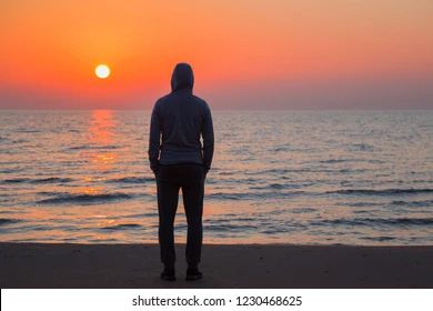 a stock image from shutterstock, of a man looking off into the ocean at sunset