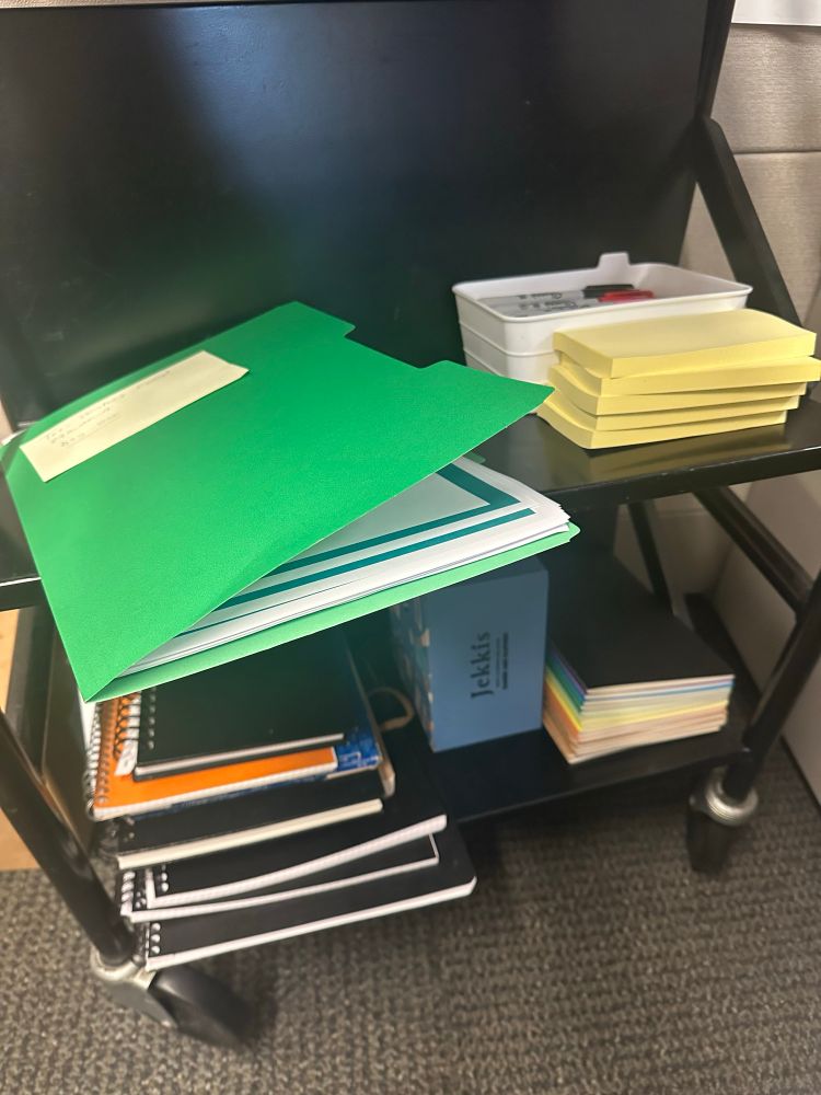 Gem’s cart next to her librarian desk— with a green folder of handouts, a stack of post its, a container of sharpies, loads of notepads. 