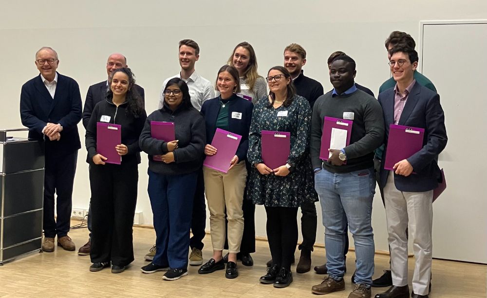 A group of 11 scientists pose for a picture after receiving their award for outstanding poster contributions and presentations. Each researcher holds a purple certificate. The dean and the co-dean of the faculty stand beside them on the left.  